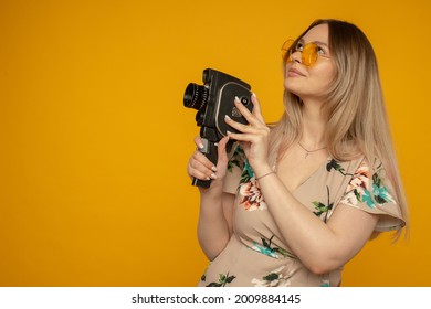 Beauty With Movie Camera. Cheerful Young Woman Holding Movie Camera And Posing Against Yellow Background