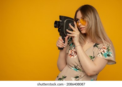 Beauty With Movie Camera. Cheerful Young Woman Holding Movie Camera And Posing Against Yellow Background