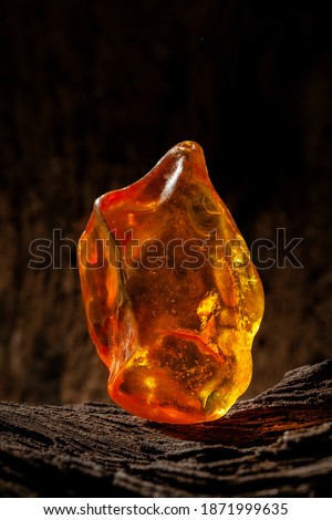 Beauty of natural raw amber. A piece of yellow opaque natural amber on large piece of dark stoned wood.