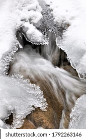 Beauty Of Nature In Winter. Closeup Of Water Flowing In Small Stream Viewed Through Hole In Melting Ice. Vertical Image.