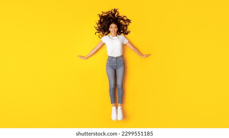 Beauty Offer. Pretty Young Lady Lying On Floor Posing Smiling At Camera Over Yellow Studio Background, Top View. Full Length Shot Of Happy Woman Wearing White T-Shirt And Skinny Jeans