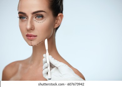 Beauty Operation. Closeup Of Beautician Hand With Scalpel Near Young Woman Face. Portrait Of Beautiful Woman With Perfect Makeup And Surgical Lines On Soft Skin. Facial Treatment. High Resolution