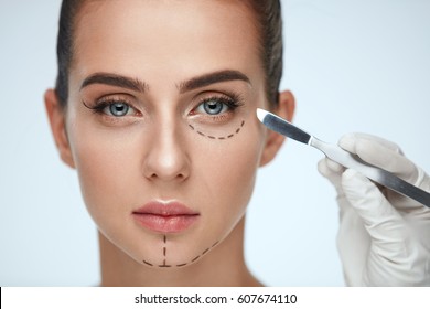 Beauty Operation. Closeup Of Beautician Hand With Scalpel Near Young Woman Face. Portrait Of Beautiful Woman With Perfect Makeup And Surgical Lines On Soft Skin. Facial Treatment. High Resolution