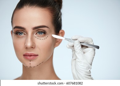 Beauty Operation. Closeup Of Beautician Hand With Scalpel Near Young Woman Face. Portrait Of Beautiful Woman With Perfect Makeup And Surgical Lines On Soft Skin. Facial Treatment. High Resolution