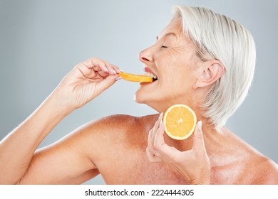 Beauty, Orange And Eating With A Mature Woman Biting Into A Fruit Slice In Studio On A Gray Background. Food, Wellness And Natural Care With A Senior Female Posing To Promote Healthy Eating Or Diet