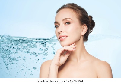 beauty, people and health concept - beautiful young woman touching her face over blue background with water splash