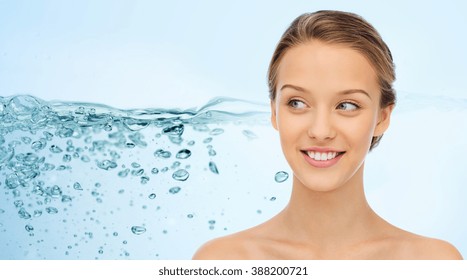 beauty, people and health concept - smiling young woman face and shoulders over water splash on blue background