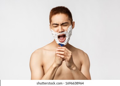 Beauty, People And Hygiene Concept. Portrait Of Carefree Handsome Asian Named Man Shaving And Singing, Get Ready In Bathroom, Apply Cream, Sing Into Razor Like Microphone, Stand White Background