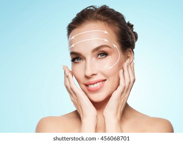 Beauty, Plastic Surgery, Facelift, People And Rejuvenation Concept - Beautiful Young Woman Touching Her Face With Lifting Arrows Over Blue Background