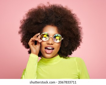 Beauty portrait of African American girl in colored holographic sunglasses. Beautiful black woman on pink background. Cosmetics, makeup and fashion