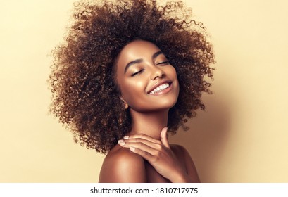 Красивый портрет афроамериканки с чистой здоровой кожей на бежевом фоне. Улыбающаяся мечтательная красивая афро-девушка.Кудрявые черные волосы