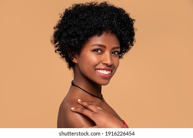 Beauty Portrait Of African American Woman With Delicate Makeup. Beige Studio Background. Smiling Beautiful Afro Girl Looking At Camera.Curly Black Hair. 