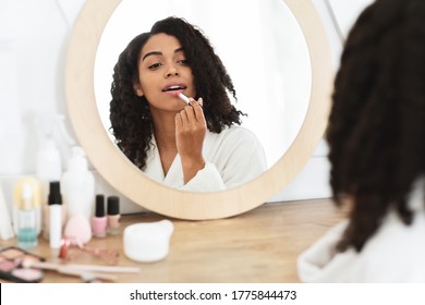 Beauty Portrait Of Attractive Black Girl Applying Pink Nude Lipstick In Front Of Mirror