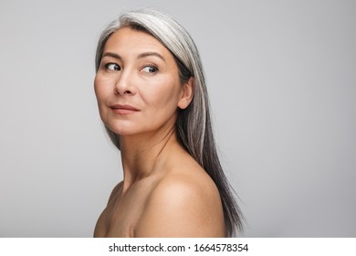 Beauty portrait of an attractive sensual mature topless woman with long gray hair standing isolated over gray background