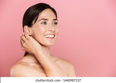Beauty portrait of an attractive smiling young topless woman standing isolated over pink background, looking away, posing - Shutterstock ID 1440987137