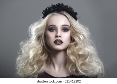 Beauty portrait of a beautiful young blonde woman with gothic make-up and decorative wreath on a gray background.