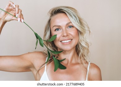 Beauty Portrait Of Blonde Hair Smiling Young Woman With Green Twig In Hand Isolated On Beige Background