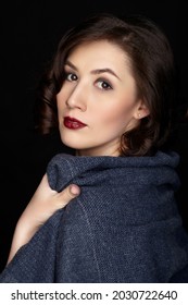 Beauty portrait of brunette woman dressed in dark blue scarf. Female portrait from a three-quarter angle on black background. Hand wraps the scarf.