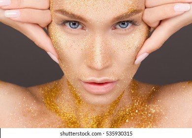 Beauty portrait of cute lovely young woman with sparkles on her face on gray background