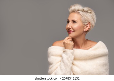Beauty portrait of elegant adult blonde woman with short hairstyle and glamour makeup. Attractive lady wearing warm fashionable sweater. A lot of copy space. Studio shot.
