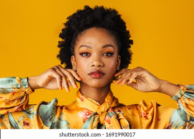 Beauty Portrait Of An Elegant  Young Woman With Orange Finger Nails Manicure, Lips And Eye Shadow, Isolated On Yellow Background