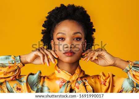 Beauty portrait of an elegant  young woman with orange finger nails manicure, lips and eye shadow, isolated on yellow background