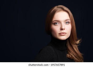 Beauty Portrait. Gorgeous Young Woman With Red Hair And Beautiful Blue Eyes Posing In Black Turtleneck On A Dark Blue Background. Studio Shot With Copy Space. 