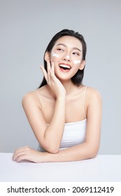 Beauty Portrait Image Of Pretty Asian Woman Smiling And Applying Face Cream Isolated Over Light Grey Background