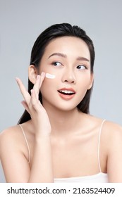 Beauty portrait image of pretty asian woman smiling and applying face cream isolated over light grey background - Shutterstock ID 2163524409