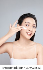 Beauty Portrait Image Of Pretty Asian Woman Smiling And Applying Face Cream Isolated Over Light Grey Background