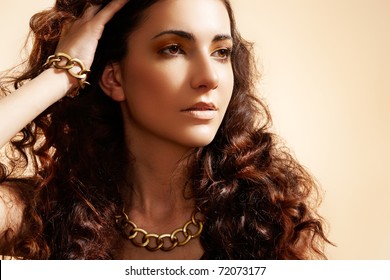 Beauty Portrait Of Luxury Fashion Woman With Glamour Gold Jewellery, Curly Hairstyle  On Beige Background. Accessories And Jewelry.