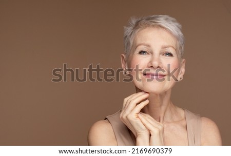 Beauty portrait of mature woman smiling with hand on face. Closeup face of happy senior woman feeling fresh after anti-aging treatment. Smiling beauty looking at camera with perfect skin.