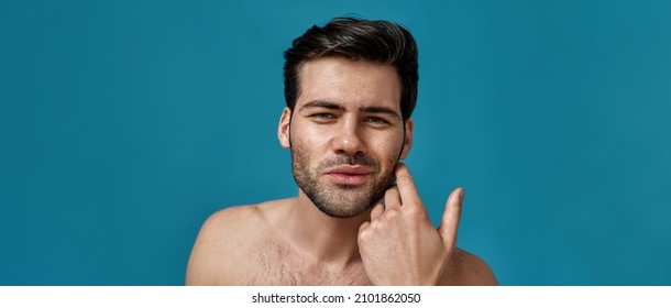 Beauty portrait of naked brunette guy touching his flawless, clean skin while posing isolated over blue background. Skin care concept. Web Banner