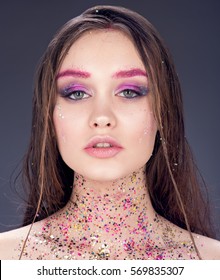 Beauty portrait of sexy young woman with wet hair. Bright professional makeup, multicolored sequins at the neck. Sensual look. Neutral dark gray background