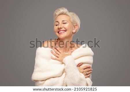 Beauty portrait of smiling adult blonde woman with short hairstyle and glamour makeup. Attractive lady wearing warm fashionable sweater. A lot of copy space. Studio shot.