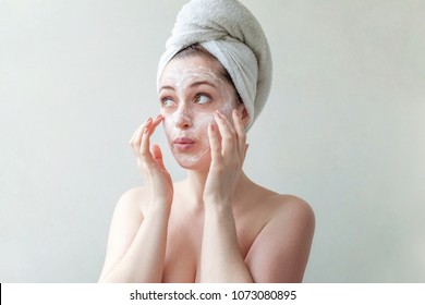 Beauty portrait of a smiling brunette woman in a towel on the head applying white nourishing mask or creme on face on white background isolated. Skincare cleansing spa relax concept