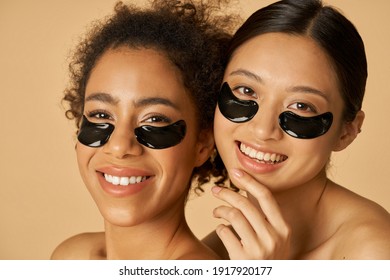 Beauty Portrait Of Two Excited Young Women Posing With Applied Black Under Eye Patches Isolated Over Beige Background