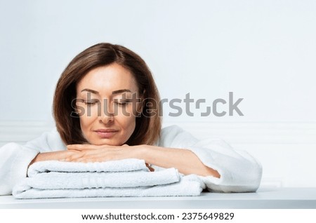 Beauty portrait of a woman in her prime, with a confident smile in housecoat resting calmly on bathroom towels