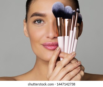 Beauty Portrait Of Woman With Makeup Brushes Near Face, Grey Background, Crop