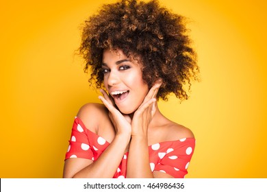 Beauty Portrait Of Young African American Girl With Afro Hairstyle. Girl Posing On Yellow Background, Looking At Camera, Smiling. Studio Shot.