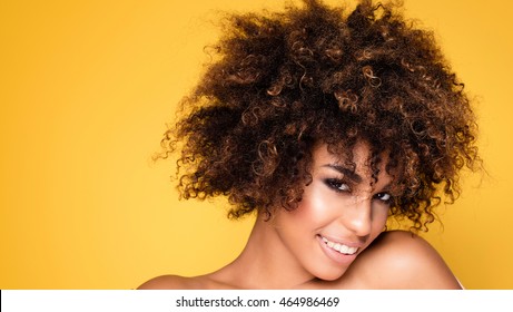 Beauty Portrait Of Young African American Girl With Afro Hairstyle. Girl Posing On Yellow Background, Looking At Camera, Smiling. Studio Shot.