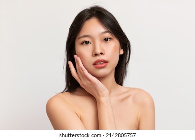 Beauty Portrait Of Young Asian Woman Touching Her Clean Face With Smooth Radiant Skin And Posing Looking At Camera Isolated On White Studio Wall. Facial Treatment. Cosmetology, Skin Care Spa Concept