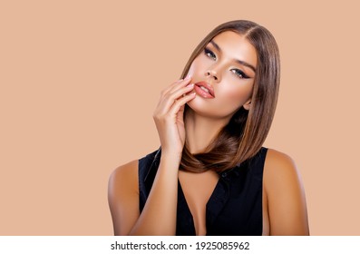 Beauty Portrait Young Woman holding her long natural brown Hair with her hands. Makeup. Brunette model with long hair posing over Beige background. Girl looking at camera. Eye  makeup,  peach lips  