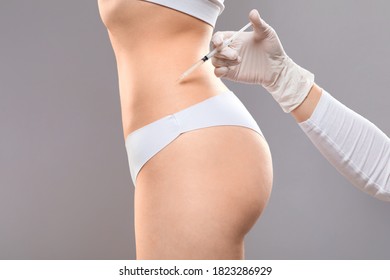 Beauty procedure for body. Slim woman having lipolysis treatment at beauty salon, closeup. Plastic surgeon making injection at belly area for unrecognizable lady, grey studio background, side view - Shutterstock ID 1823286929