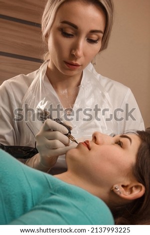 beauty procedure. close up permanent tattoo. blonde female master in white medical gloves makes permanent eyebrow tattoo on a brunette model girl. beauty concept, free space