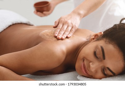 Beauty Procedures At Spa. Masseuse Applying Body Scrub On Black Girl Back, Closeup