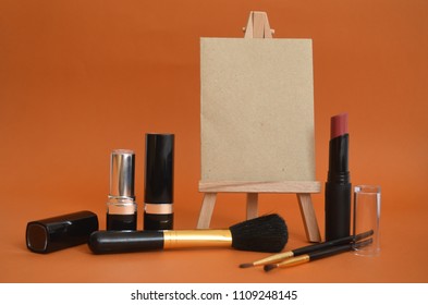 Beauty Products For Make Up And Blank Paper On Easel For Working Hours Or Price List, Copy Space. Makeup Supplies On Orange Background.