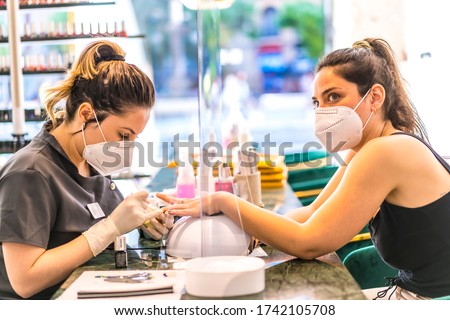 Beauty salon worker with face mask painting colorful nails on brunette Caucasian client. Reopening after the corod-19 pandemic. Manicure and Pedicure Salon. Coronavirus