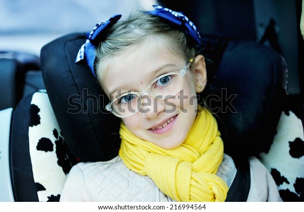Beauty school aged kid girl in glasses and\
yellow scarf in the car seat with\
belt
