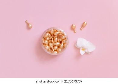Beauty serum capsules in a jar near orchid flower on light pink top view. Skincare beauty product. Facial cosmetics, pastel minimal composition